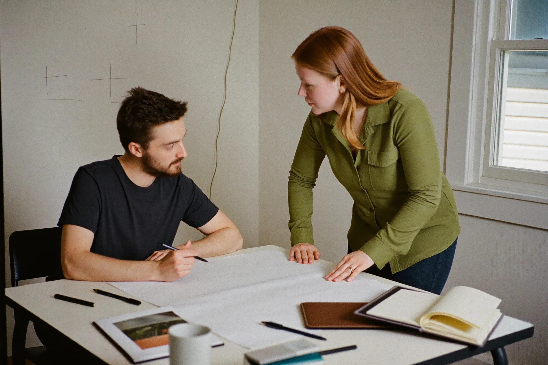 A consultant talking a client through plans laid out on a work table